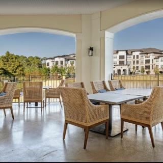 A spacious patio area overlooking an apartment complex, featuring a dining table with wicker chairs.
