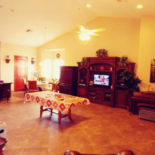 A cozy living room featuring a central table with a patterned cover, a large wooden entertainment unit with a television, and comfortable seating.