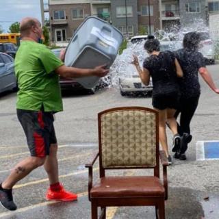 A man playfully dumps a bucket of water on two women in a parking lot.