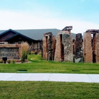 A view of a stone monument beside a modern building, set in a green landscape.