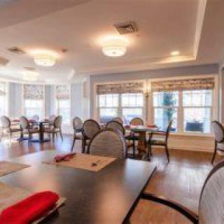 A bright dining room with multiple tables and chairs, featuring large windows allowing natural light to fill the space.