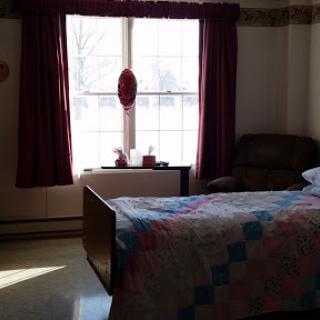 A cozy bedroom with a neatly made bed and natural light streaming through the window.