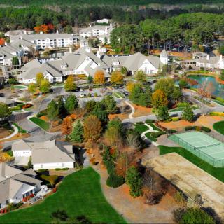 Aerial view of a residential area with tennis courts and swimming pools surrounded by trees and buildings.