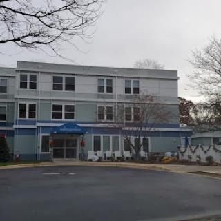 A three-story commercial building with a blue awning, set against a cloudy sky.