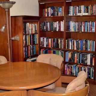 A cozy library corner featuring wooden bookshelves filled with books, a round table, and comfortable chairs.