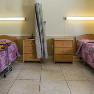 A hospital room with two beds separated by a curtain and nightstands beside each bed.