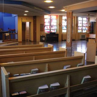 Interior view of a church with wooden pews and large windows.