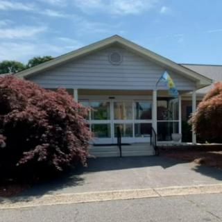A small building with a front entrance, surrounded by trees and underneath a clear blue sky.