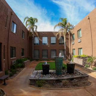 A serene courtyard with a central fountain, surrounded by palm trees and a two-story brick building.