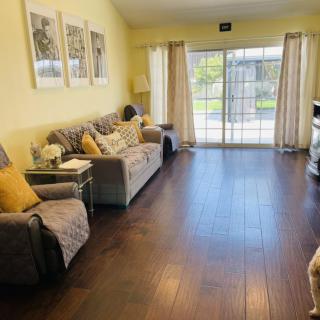 A cozy living room with a sofa and wooden flooring, featuring artwork on the wall and a sliding glass door leading outside.