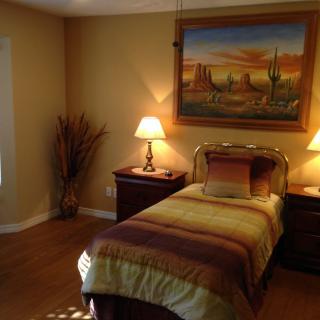 A cozy bedroom with a single bed, two nightstands with lamps, and a desert-themed painting on the wall.