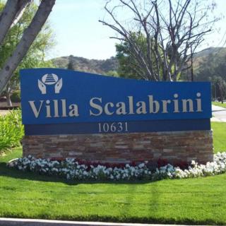 A blue entrance sign for Villa Scalabrini with well-maintained landscaping.