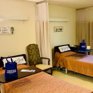 A view of a patient room with two beds, a chair, and medical furniture.