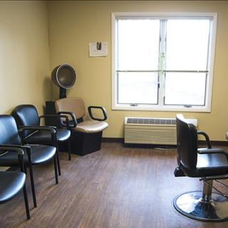 A small waiting area in a barber shop with chairs and a salon chair near the window.