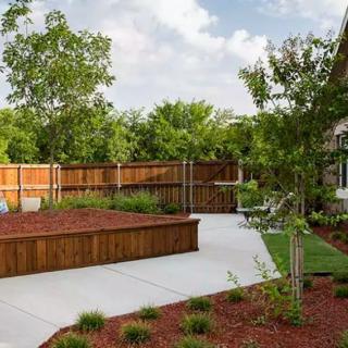 A well-maintained backyard featuring a paved path, wooden fence, and lush landscaping with trees and mulch.