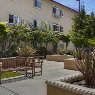 A peaceful courtyard with benches and lush greenery in front of a residential building.