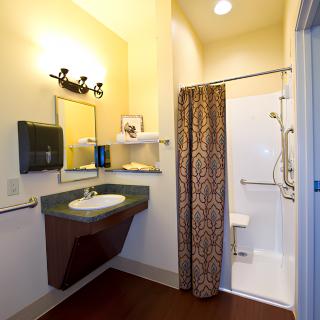 An accessible bathroom with a sink, shower, and curtain, featuring shelves and lighting.
