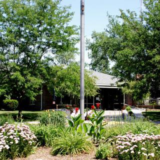 A scenic garden with a flagpole, surrounded by flowers and trees in front of a building.