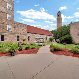 A courtyard with a pathway leading to buildings and a tall tower under a blue sky with clouds.