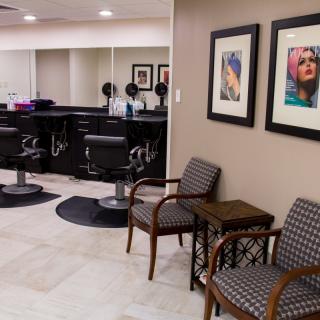 A modern hair salon interior featuring styling stations, comfortable waiting chairs, and framed artwork on the walls.