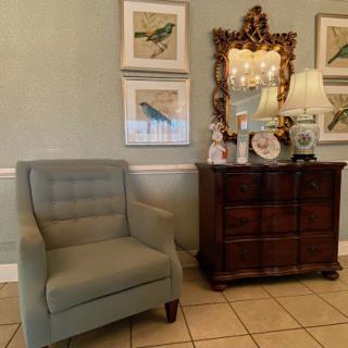 A cozy corner showcasing a blue chair beside a stylish dresser, adorned with decorative items and framed art.
