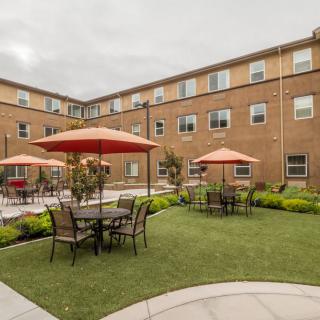 A courtyard with tables and umbrellas, surrounded by a brick building.