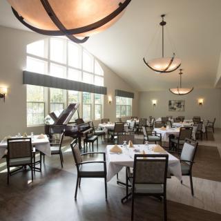 A spacious and elegantly designed restaurant interior with neatly arranged tables and chairs, large windows, and a grand piano in the corner.