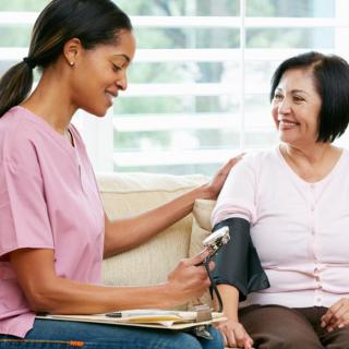 A healthcare professional taking a patient's blood pressure during a home visit.
