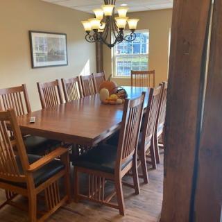 A dining room with a large wooden table surrounded by chairs, illuminated by a chandelier.