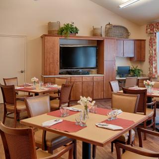A neatly arranged dining room with wooden tables and chairs, adorned with placemats and flower arrangements.