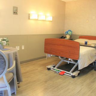 A well-lit hospital room featuring a patient bed, a small table with chairs, and warm decor.
