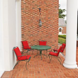 An inviting outdoor patio area with red cushioned chairs and a green table set against a brick wall.