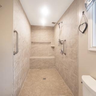 A modern walk-in shower with neutral tiles, featuring grab bars and a built-in bench.