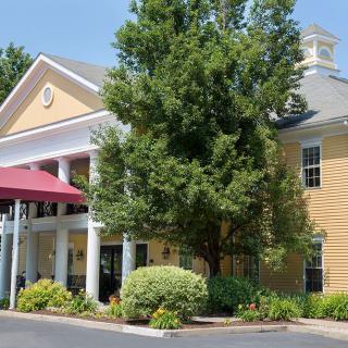 A picturesque building with a columned entrance surrounded by lush trees and landscaping.