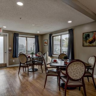 A cozy dining area with tables and chairs, featuring large windows and wooden flooring.