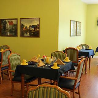 A cozy dining area with tables set for guests, featuring striped chairs and paintings on yellow walls.