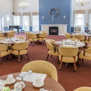 A spacious dining room with neatly set tables and a fireplace in a well-lit setting.