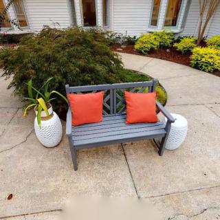 An inviting outdoor bench with orange cushions surrounded by greenery and potted plants.