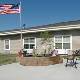 A building exterior with an American flag flying, featuring a landscaped patio area with benches.