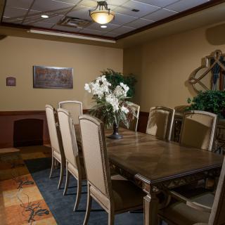 A cozy dining room with a large table, surrounded by chairs, decorated with flowers and plants.