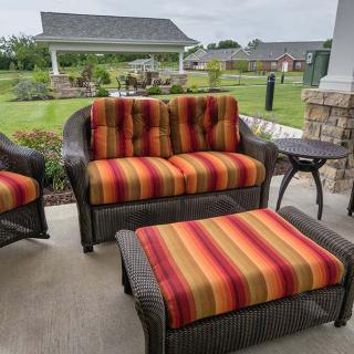 A cozy patio setup featuring wicker furniture with vibrant red and orange striped cushions, set against a lush garden backdrop.