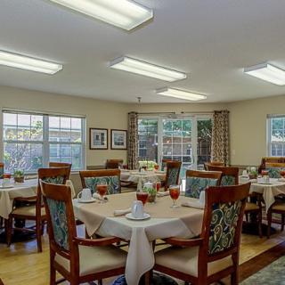 A well-lit dining room with set tables and chairs, featuring large windows and decorative elements.