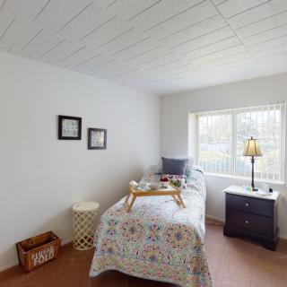A bright and minimalist bedroom with a single bed, side table, and a lamp by the window.