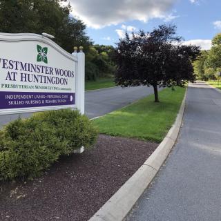 Entrance sign for Westminster Woods at Huntingdon, surrounded by trees and a road.