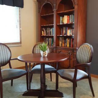 A cozy reading nook featuring a wooden table, elegant chairs, and a bookshelf filled with books.