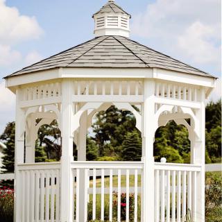 A white gazebo set in a garden with lush greenery and a clear sky.