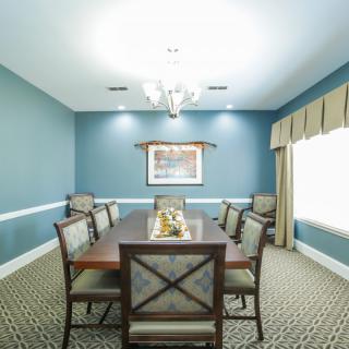 A well-lit dining room with a large table and six chairs, decorated with a chandelier and wall art.