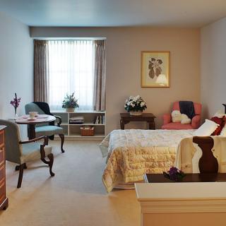 A cozy bedroom with a bed, chairs, and a window allowing natural light.