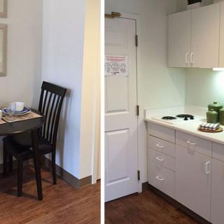 A compact apartment kitchen and dining area with a small table and chairs, featuring minimalistic cabinets and appliances.
