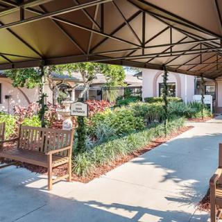 A serene outdoor setting featuring benches under a canopy alongside a landscaped pathway.